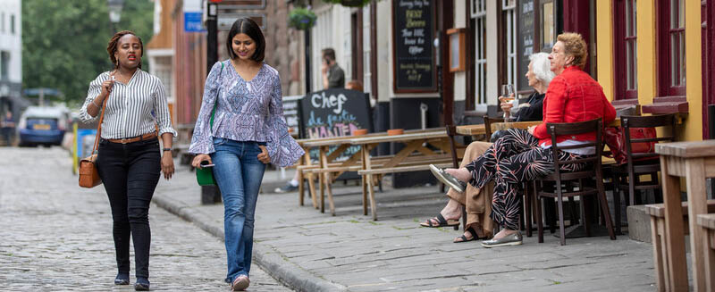people sit outside of bars on king street while a few people walk past down the paved street